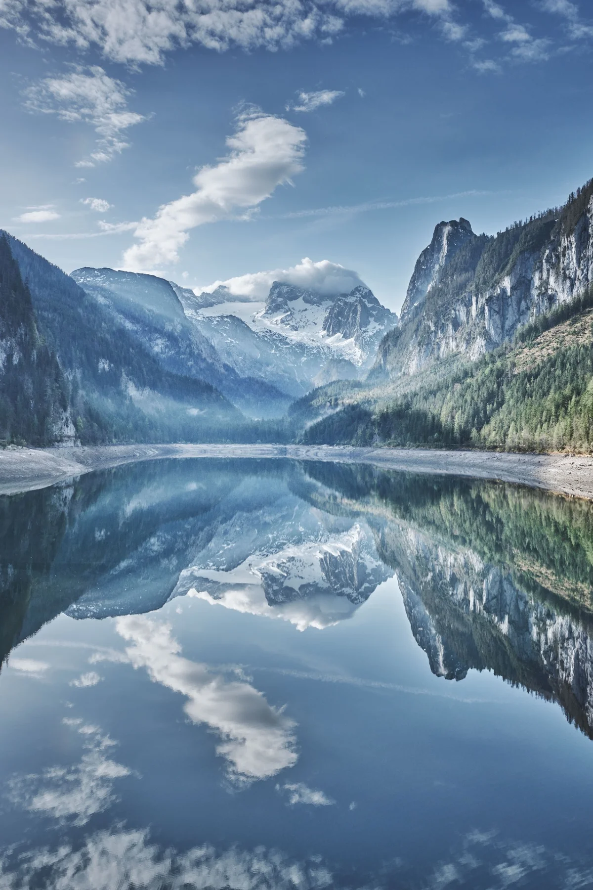 Snow-covered mountains and forested cliffs reflected in a still alpine lake.